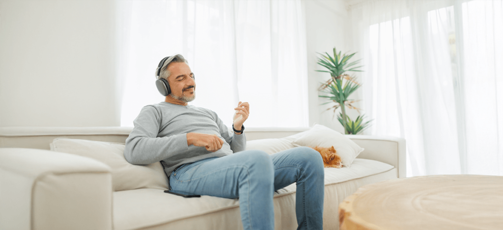 Man unwinds with music on sofa beside resting cat in a living room